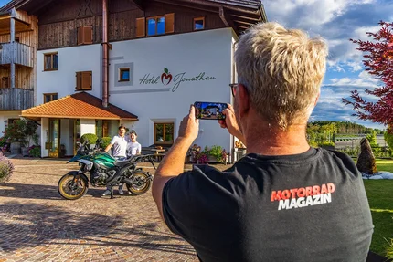 Person taking photo of motorcycle with two people in front of Hotel Jonathan