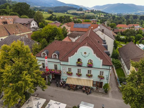 Altes Gasthaus mit blauen Fassade und Blumen in einem Dorf mit Bergen im Hintergrund