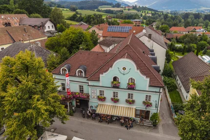 Altes Gasthaus mit blauen Fassade und Blumen in einem Dorf mit Bergen im Hintergrund
