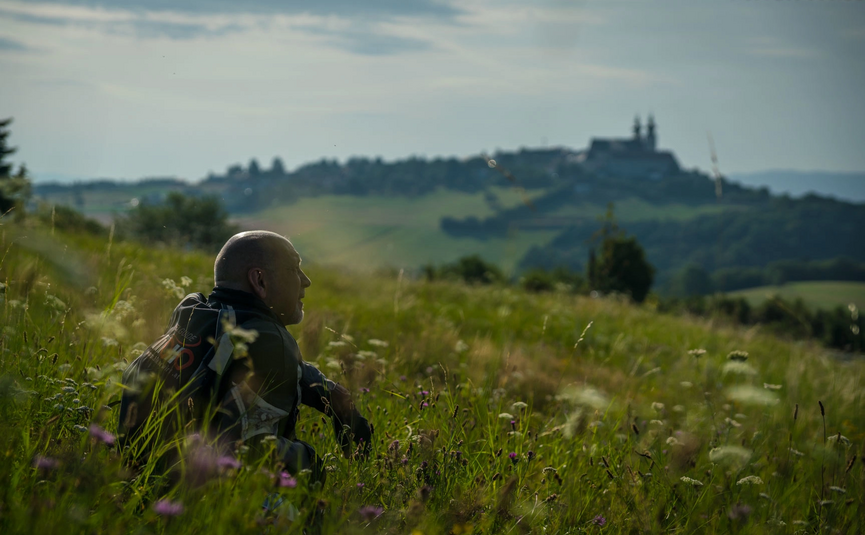 Wachau Maria Taferl 250 km Man sitting in a meadow looking at a hill with a monastery.