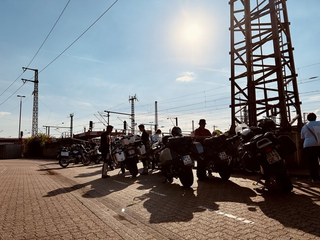 Motorrad- und Autoreisezug © Eduard Bopp Motorradfahrer stehen neben ihren Motorrädern unter Sonnenlicht am Bahnsteig