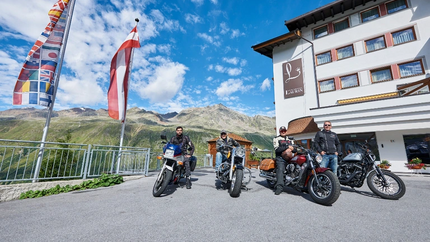 Zum Südtiroler Wein Vier Motorradfahrer vor einem Hotel mit Bergblick und Fahnen