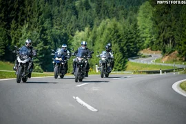 Four motorcyclists riding on a country road with forest background