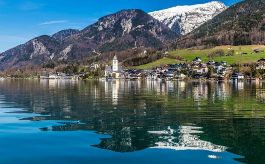 Dorf am See mit Bergen und schneebedecktem Gipfel im Hintergrund