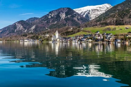 Village by lake with mountains and snow-covered peak in the background
