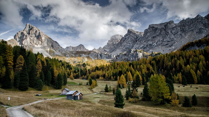 Wanderweg zu Hütten vor bewaldeten Bergen unter bewölktem Himmel