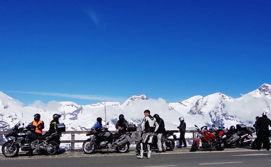 King of the curves offer - as of € 218,- per person Motorcyclists stop by a snowy mountain range under clear blue sky