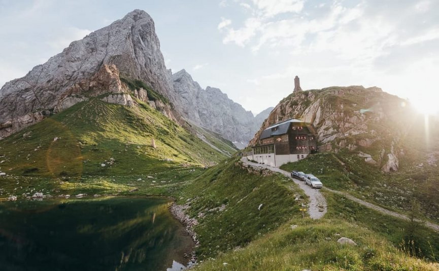 Bergwachthuis bij een meer met steile rotsachtige pieken in zonlicht
