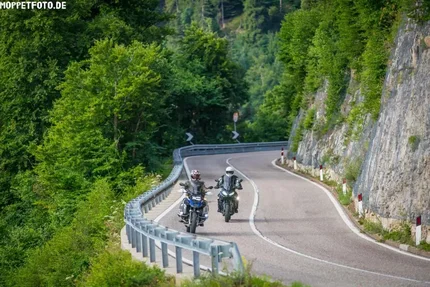14. Jaufenpass & Penserjoch Zwei Motorradfahrer fahren auf kurviger Bergstraße neben Felswand und Wald.