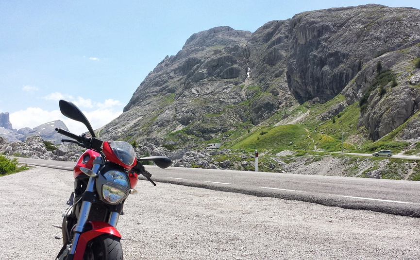 Rode motorfiets geparkeerd op bergweg met rotsachtige kliffen en groene hellingen