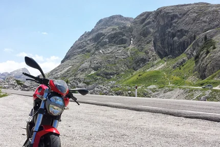 Red motorcycle parked on mountain road with rocky cliffs and green slopes