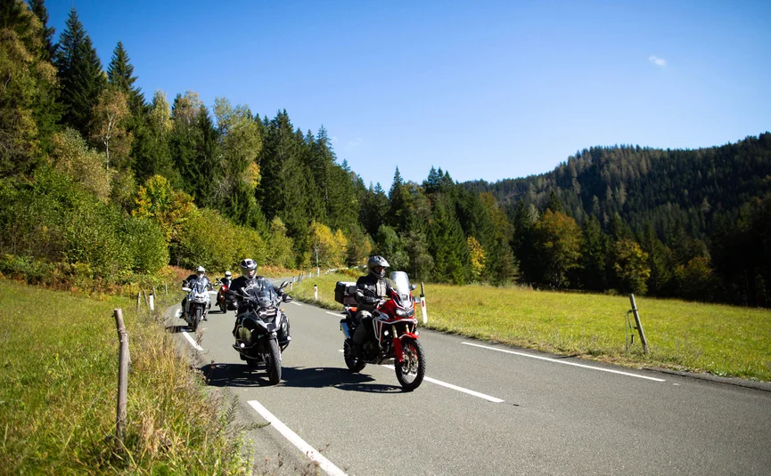 Motorcyclists riding on a country road through forested mountains