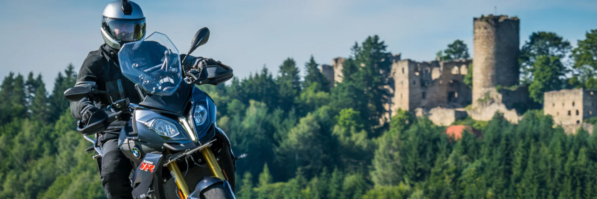Motorcyclist on country road with forested hill and castle ruins