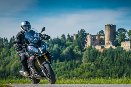 Motorradfahrer auf Landstraße vor bewaldetem Hügel mit Burgruine