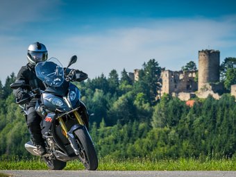 Motorradfahrer auf Landstraße vor bewaldetem Hügel mit Burgruine