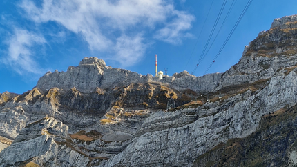 Berg mit Felswänden, grünem Baum und Seilbahn unter blauem Himmel