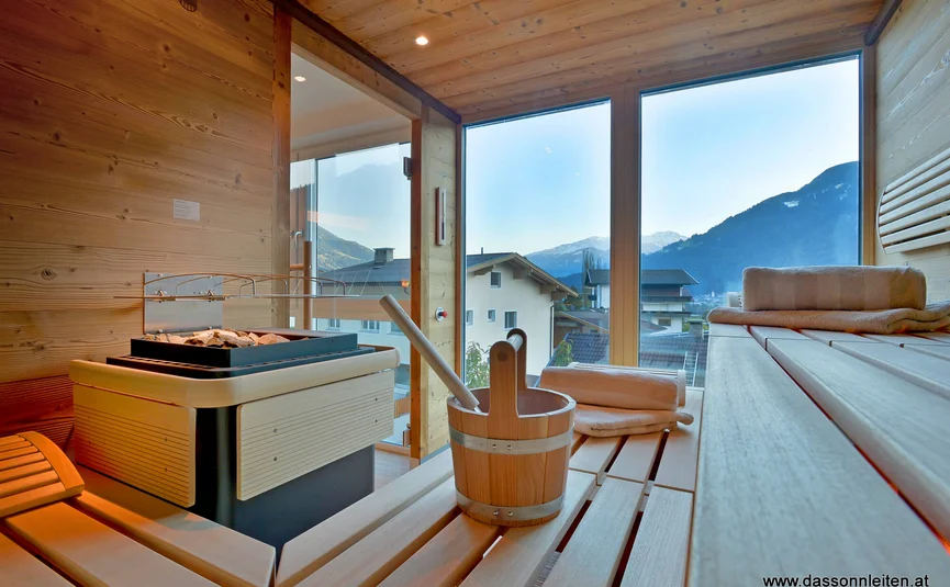 Sauna with wooden benches and view of mountains and houses through glass windows
