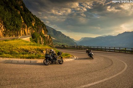 Zwei Motorradfahrer fahren eine kurvige Bergstraße bei Sonnenuntergang