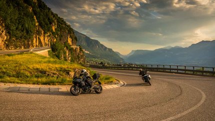 Twee motorrijders op een kronkelende bergweg bij zonsondergang