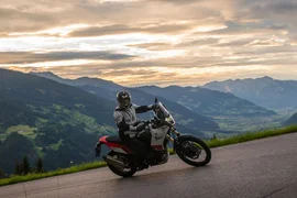 Motorradfahrer auf Bergstraße mit Tal und Bergen bei Sonnenuntergang