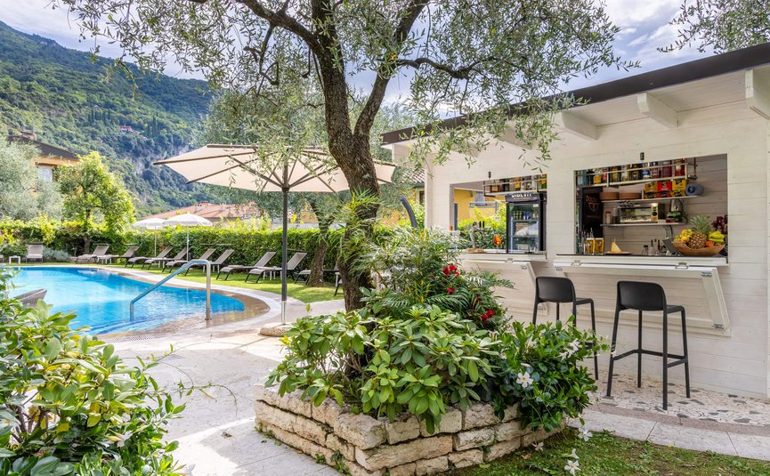 Pool area with loungers, umbrellas, and bar in a lush garden