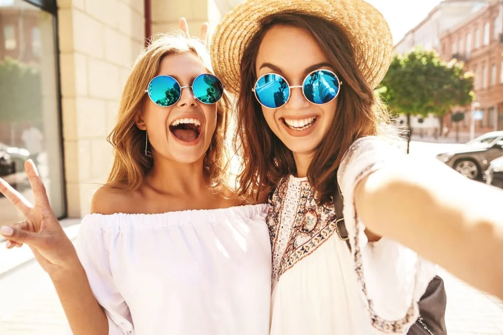 Twee lachende jonge vrouwen met zonnebrillen maken buiten een selfie