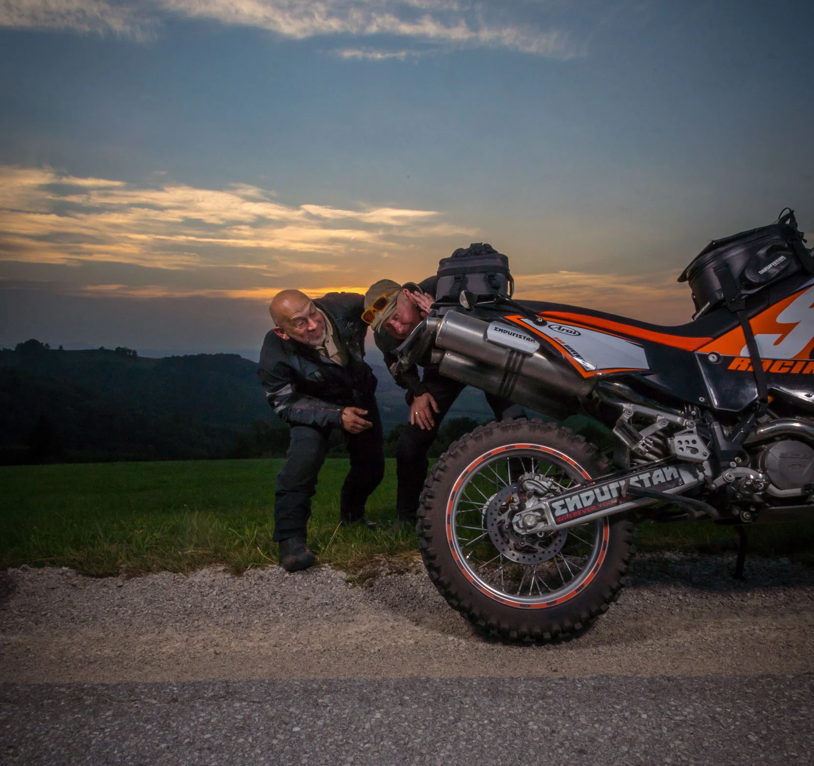 Fahr ruhig & rücksichtsvoll! © Moppetfoto.de Zwei Männer schauen hinter ein Motorrad am Straßenrand bei Sonnenuntergang