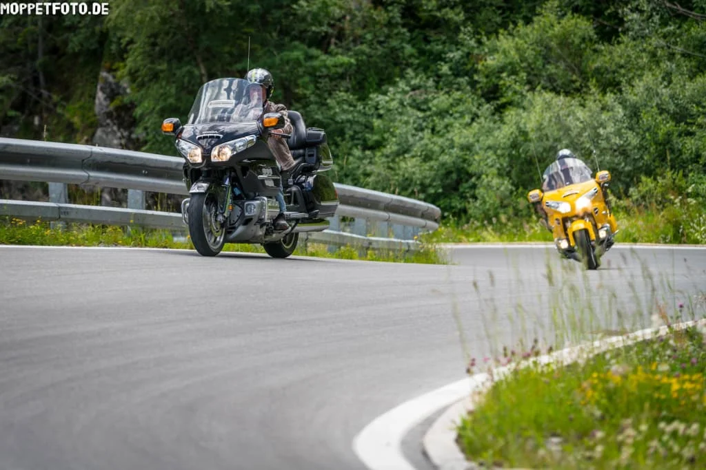 Zwei Motorradfahrer auf kurviger Bergstraße mit grüner Vegetation
