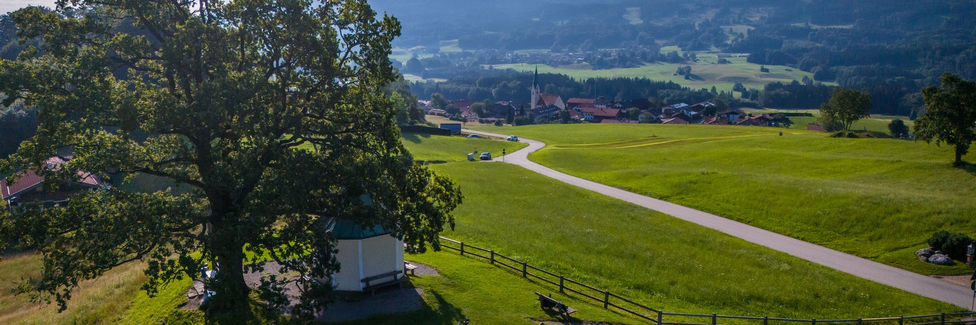 Gasthof Hotel Zur Post Samerberg *** © Moppetfoto.de Fahrradfahrer am großen Baum auf grünem Hügel mit Dorf und Bergen im Hintergrund