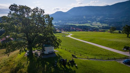 Region Rosenheim - Oberbayern © Moppetfoto.de Fahrradfahrer am großen Baum auf grünem Hügel mit Dorf und Bergen im Hintergrund
