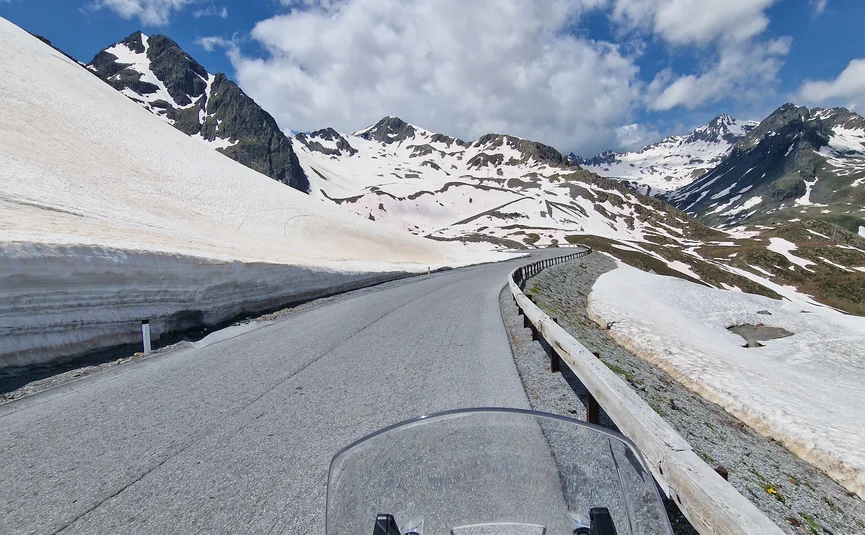 View from motorcycle on mountain road with snow and cloudy sky