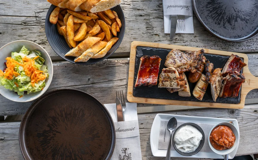 Grilled meat, potato wedges, bread, salad and dips on wooden table
