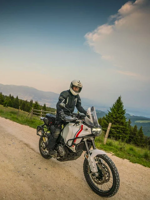 Motorcyclist riding on gravel road in mountainous area with trees