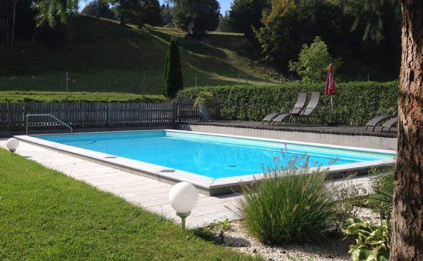 klare outdoor-pool mit liegestühlen und hügeliger waldlandschaft