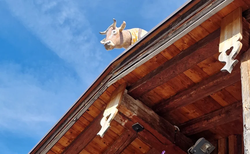 Wooden balcony with flower box and cow sculpture on roof against blue sky