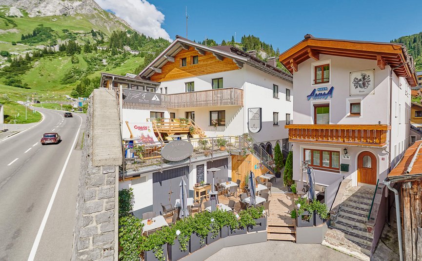 Haus Flexen © Mathies Wilhelm Robert jun. Gastgarten mit Tischen und Stühlen vor Häusern in Alpenlandschaft