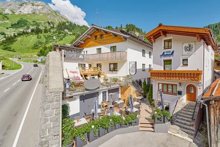Gastgarten mit Tischen und Stühlen vor Häusern in Alpenlandschaft