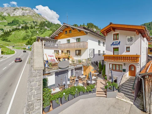 Gastgarten mit Tischen und Stühlen vor Häusern in Alpenlandschaft