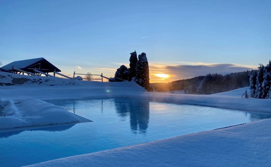 Beheizter Pool umgeben von Schnee bei Sonnenuntergang