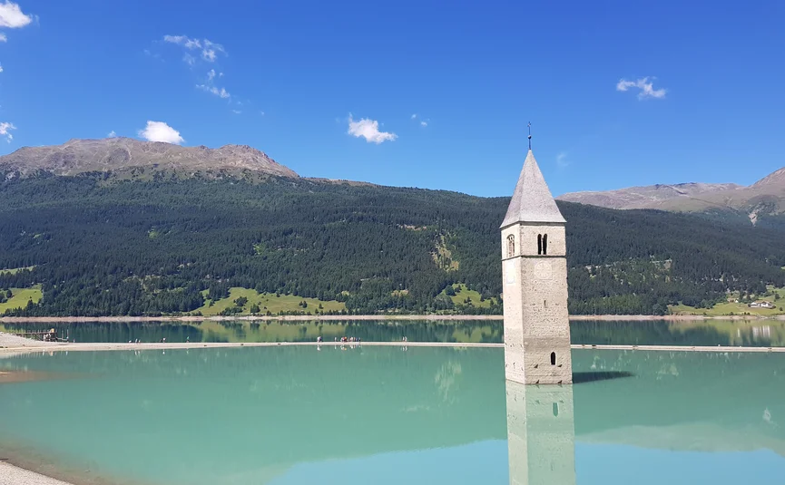 Church tower rising from a lake with mountains and blue sky