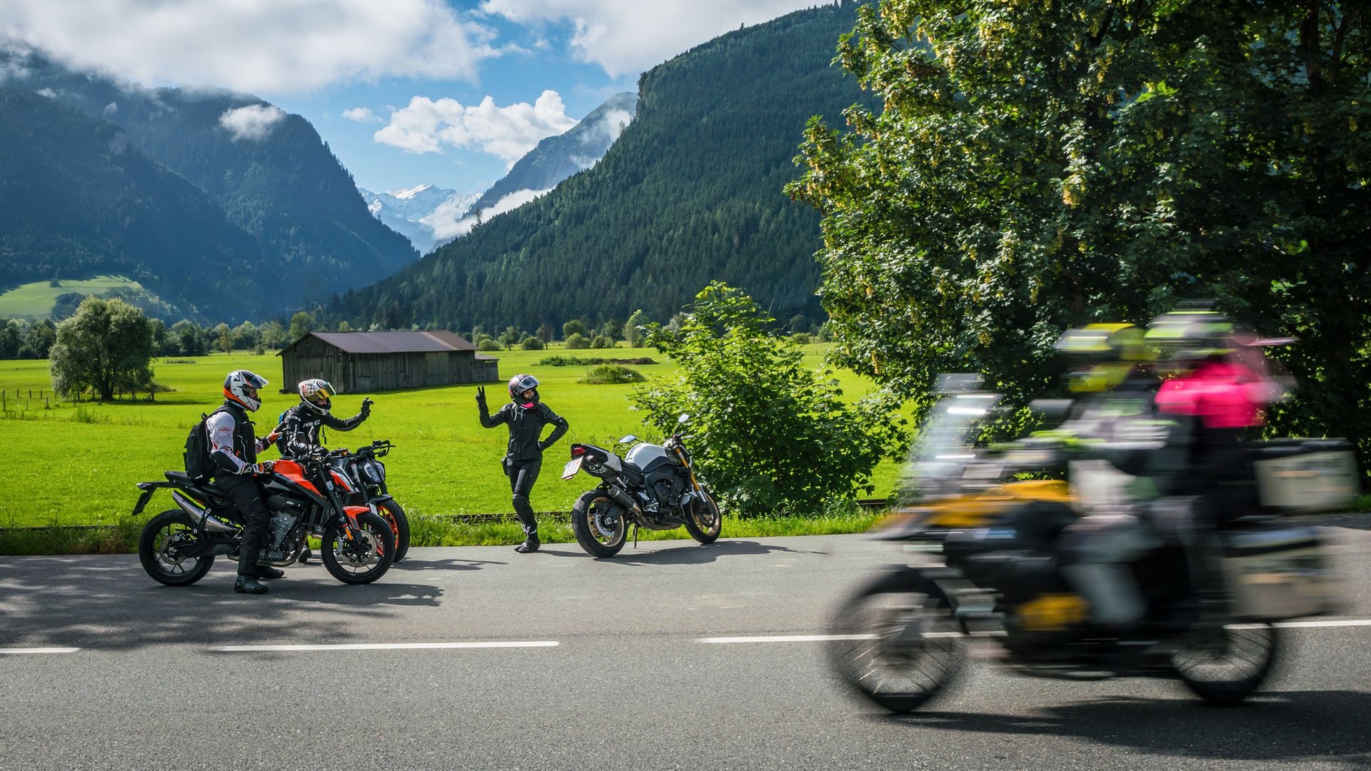 Motorradfahrer vor Berglandschaft mit grünen Wiesen und blauem Himmel