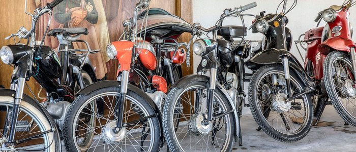 Mehrere alte Mopeds stehen nebeneinander in einer Garage vor einem Wandbild