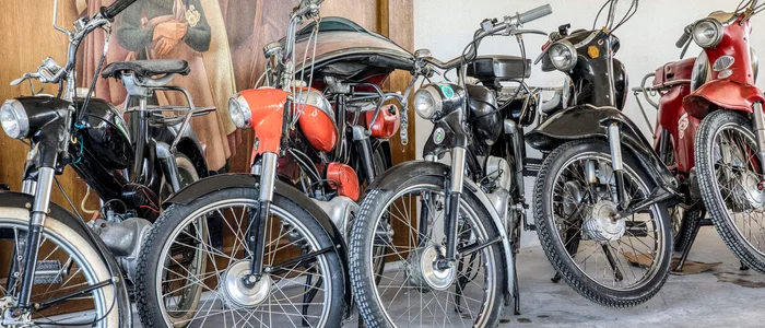 Meerdere oude bromfietsen naast elkaar in een garage voor een muurschildering