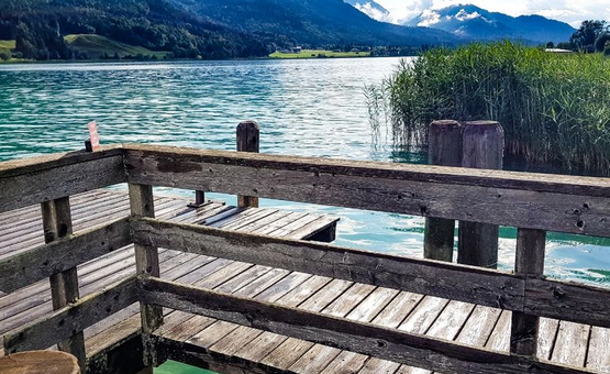 Holzsteg am See mit Bergen und grüner Vegetation im Hintergrund