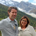 A man and a woman smiling with forest and snowy mountain in background