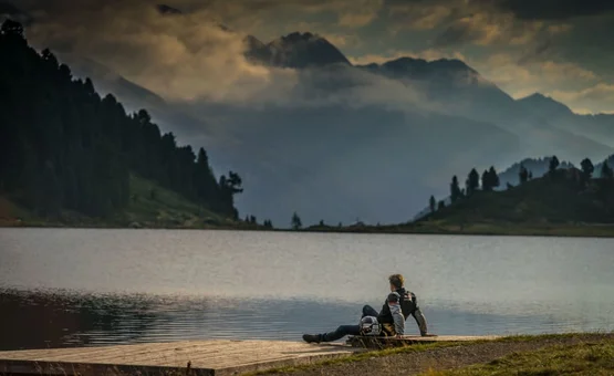 Moar's Bike & Relax Week Twee mensen zitten aan een bergmeer met bergen op de achtergrond