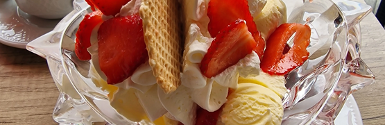 Eisbecher mit Erdbeeren, Sahne und Waffeln auf einem weißen Teller