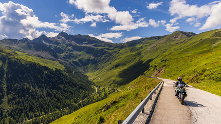 Motorradfahrer auf Bergstraße mit grünem Tal und Bergen unter blauem Himmel