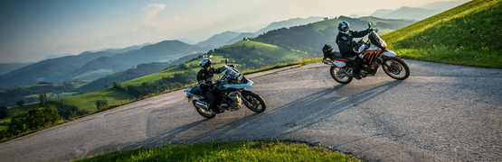 Two motorcyclists on mountain road with green hills and blue sky