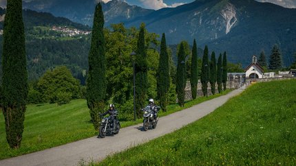 Friaul – Julisch Venetien © Moppetfoto.de Zwei Motorradfahrer fahren auf einem Weg mit Bäumen und Bergen im Hintergrund